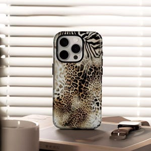 May include: A smartphone case with a mixed animal print design. The case features a combination of leopard spots and zebra stripes in shades of brown, tan, and black. The case has a black border and a camera cutout.