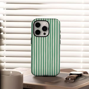 May include: A smartphone case featuring a green and white striped design. The case has a black camera module and black side buttons. The case is on a book next to a watch with a brown leather strap.