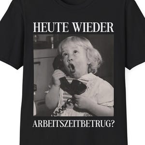 May include: Black t-shirt featuring a vintage black and white image of a surprised child holding a telephone. The text "HEUTE WIEDER" is above the image, and "ARBEITSZEITBETRUG?" is below. A humorous design.