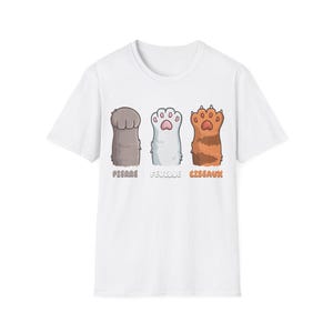 以下が含まれることがあります： 白いTシャツに、3匹の漫画の猫の足の遊び心のあるデザインが施されています。 足はグレー、白、オレンジの色合いで、その下に「PIERRE」、「FEUILLE」、「CISEAUX」という言葉が遊び心のあるフォントで印刷されています。