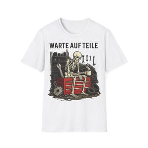 Könnte beinhalten: Weißes T-Shirt mit einem Cartoon-Skelett, das auf einer roten Werkzeugkiste sitzt und eine Tasse hält. Das Skelett ist von Werkzeugen und Autoteilen umgeben. Der Text "WARTE AUF TEILE" ist darüber gedruckt. Das Design hat ein Mechaniker-Thema.