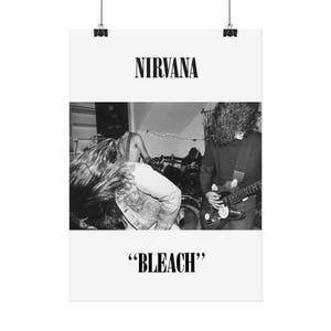 Peut inclure: Affiche en noir et blanc représentant le groupe Nirvana en concert. Le mot « NIRVANA » est imprimé en haut et le mot « BLEACH » en bas.