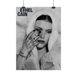 Puede incluir: Póster en blanco y negro con el texto "ETHEL CAIN". La imagen muestra a una persona con cabello oscuro y un velo blanco, con tatuajes en la mano. La persona se está tocando la cara.