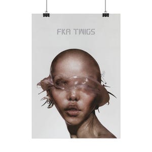 Può includere: Un poster con un ritratto di una persona con la testa rasata e una forma amorfa traslucida che oscura gli occhi. Il testo "FKA TWIGS" è stampato in grigio in alto. L'immagine è attaccata al muro con clip nere.
