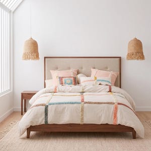 Puede incluir: Un dormitorio con una cama de madera y un cabecero beige. La cama está hecha con una funda nórdica crema adornada con rayas coloridas y texturizadas. Cojines a juego y una alfombra tejida completan el espacio acogedor.