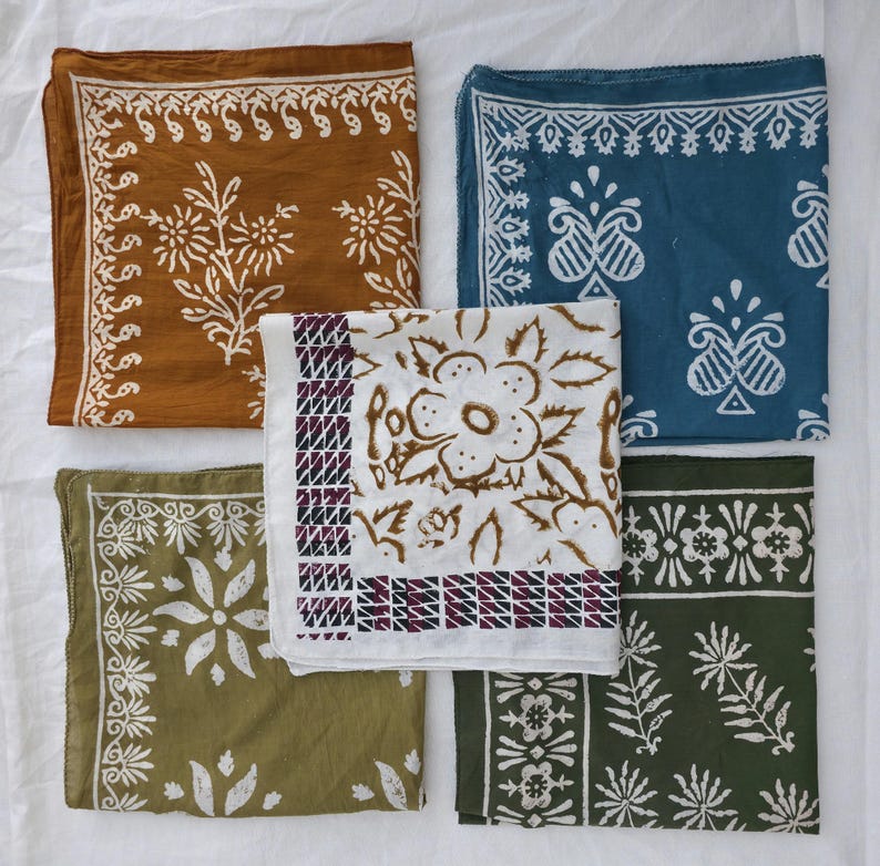 May include: Five square bandanas in shades of brown, blue, green, and white, each featuring a unique floral or geometric pattern in contrasting colors. The bandanas are arranged on a white surface.