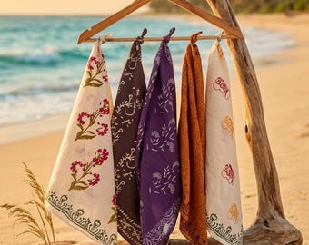 Peut inclure: Cinq bandanas colorés, crème, marron, violet, orange et blanc cassé, sont suspendus à un présentoir en bois sur une plage. Chaque bandana présente un motif floral ou cachemire unique. Le présentoir est fait de bois flotté et d'un cintre en bois.