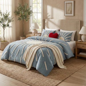 Pode incluir: Um conjunto de edredão azul com um design de sol, com detalhes brancos texturizados. O conjunto inclui fronhas a condizer com desenhos de sol e uma almofada vermelha em forma de coração. Uma manta creme está sobre a cama.