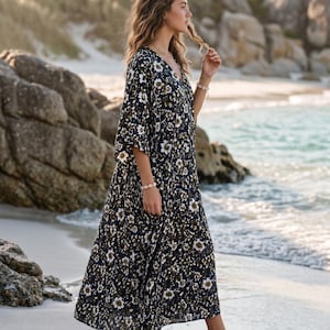 May include: A floor-length kaftan dress featuring a dark navy blue base with an all-over floral pattern in shades of white, cream, and olive green. The garment has a V-neckline, loose-fitting elbow-length sleeves, and a relaxed, flowing silhouette.