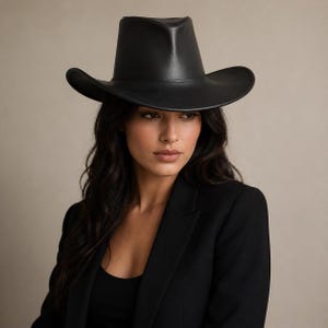 Puede incluir: Un sombrero de vaquero negro con ala ancha. El sombrero est&aacute; hecho de un material liso y tiene un dise&ntilde;o occidental cl&aacute;sico. Es un accesorio elegante.