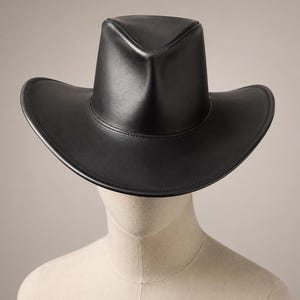Puede incluir: Un sombrero de vaquero de cuero negro con ala ancha y corona estructurada. El sombrero se exhibe en una cabeza de maniqu&iacute;. El ala del sombrero mide aproximadamente 38 cm de di&aacute;metro.
