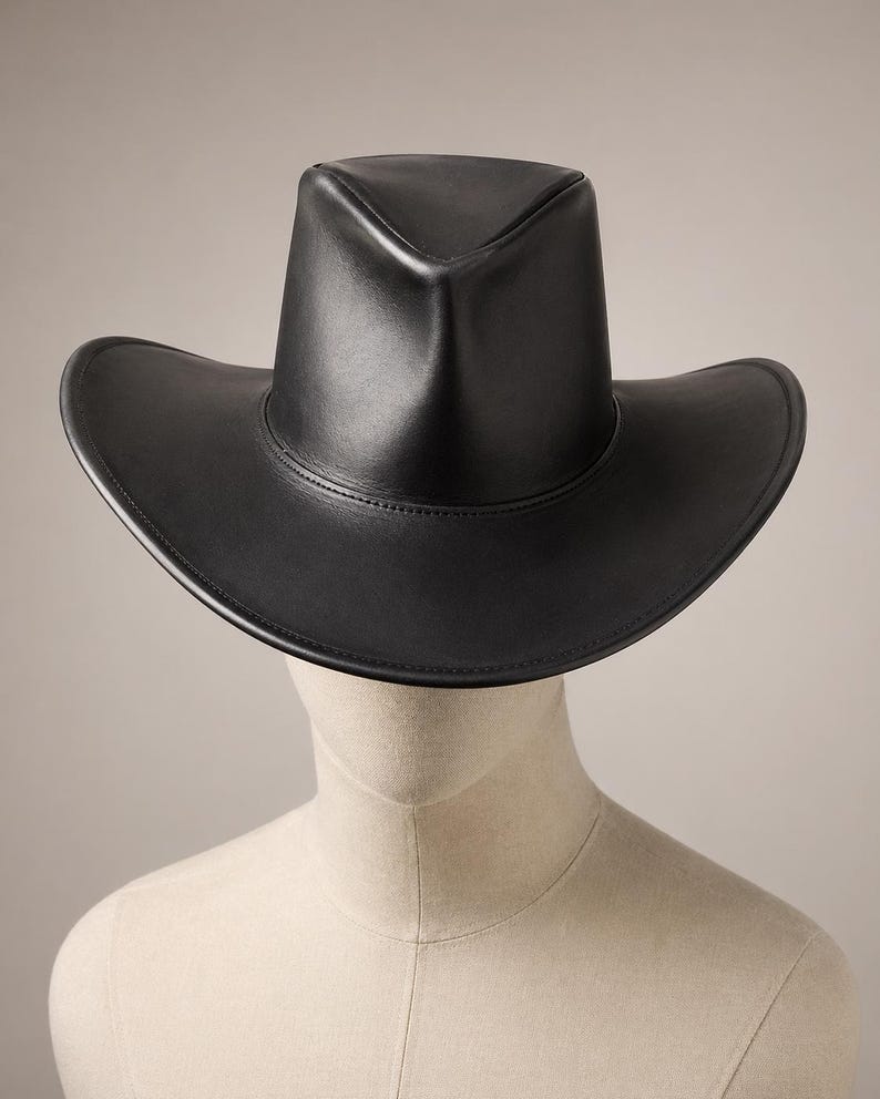 Puede incluir: Un sombrero de vaquero de cuero negro con ala ancha y corona estructurada. El sombrero se exhibe en una cabeza de maniqu&iacute;. El ala del sombrero mide aproximadamente 38 cm de di&aacute;metro.