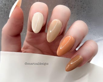 May include: A hand displaying a set of long, almond-shaped nails painted in a gradient of neutral colors. The colors include off-white, beige, light brown, orange-brown, and dark brown. The text "@smartnaildesigns" is visible.
