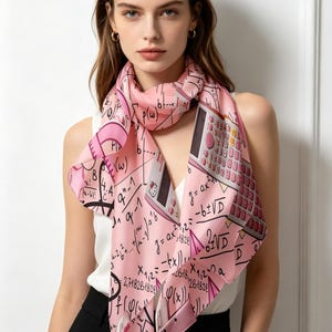 Può includere: Una sciarpa di seta rosa con un motivo ripetuto di equazioni matematiche e un design a calcolatrice. La sciarpa ha un bordo rosa scuro ed è drappeggiata intorno al collo.