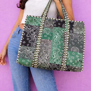 Puede incluir: Un bolso tote rectangular grande con un diseño de patchwork acolchado en tonos verde bosque, gris carbón y negro. La tela muestra un patrón de bandana de cachemira repetitivo con detalles en blanco y dos correas resistentes.