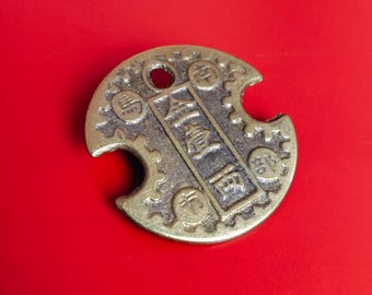 May include: A bronze-colored, circular coin with a hole at the top and a bite taken out of the side. The coin has Chinese characters in the center and a gear-like design around the edge. The coin is set against a bright red background.
