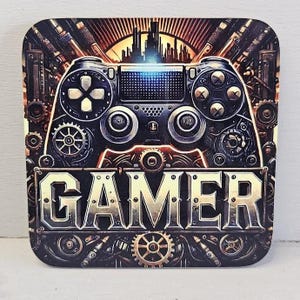 Könnte beinhalten: Quadratischer Untersetzer mit einem Design im Steampunk-Stil, das einen Gamecontroller und das Wort „GAMER“ in einer metallischen Schrift zeigt. Das Design beinhaltet Zahnräder, Nieten und eine Stadtsilhouette in Braun-, Gold- und Schwarztönen.