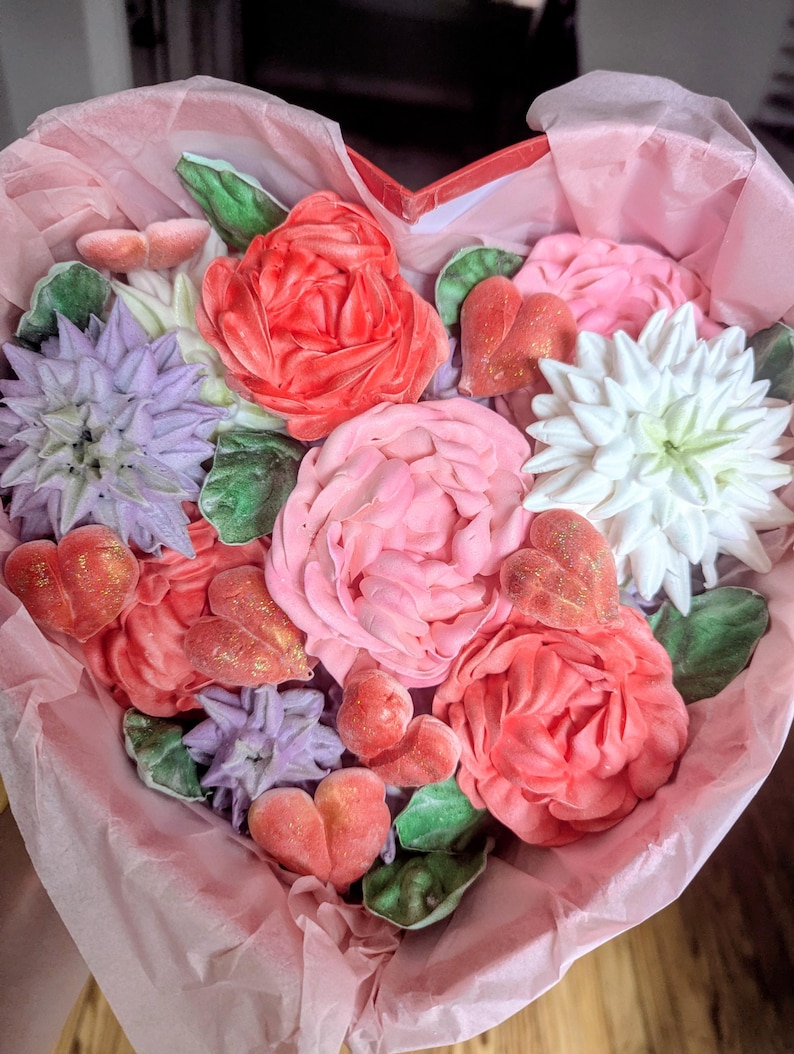 May include: A heart-shaped box filled with decorative floral-shaped confections in shades of red, pink, white, and purple. The arrangement includes detailed flower blossoms, green leaves, and small heart-shaped pieces with a gold glitter finish.