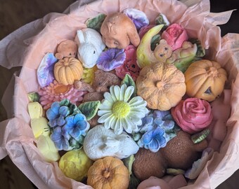 May include: A round container lined with light pink tissue paper, filled with an assortment of small, moulded figures including orange pumpkins, white and brown rabbits, teddy bears, and various colourful flowers like daisies and roses.
