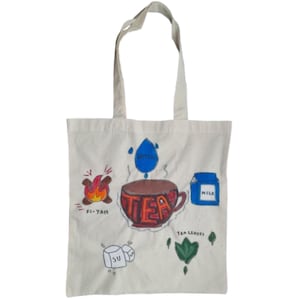 May include: Off-white tote bag featuring a tea-themed illustration. The design includes a cup of tea, a flame, a water droplet, a milk carton, tea leaves, and sugar cubes. The word "TEA" is written on the cup.