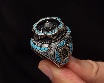 May include: A detailed silver ring with turquoise gemstones. The ring features an ornate design with a central dome-shaped element and a border of turquoise stones. The ring has an engraved pattern and a gold-colored accent.