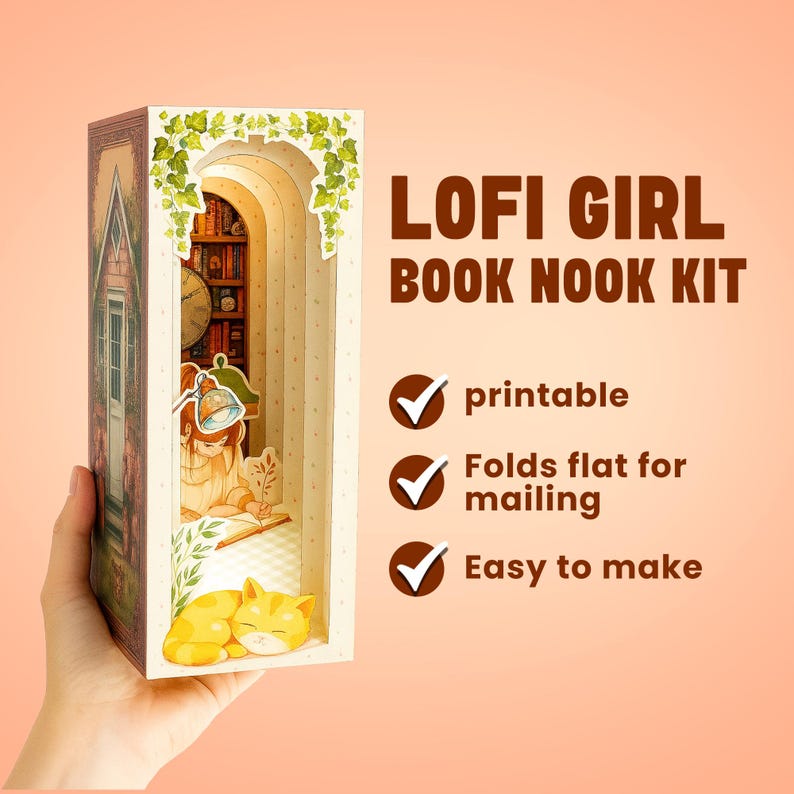 Puede incluir: Un "LOFI GIRL BOOK NOOK KIT" se sostiene en una mano. El kit presenta una escena en miniatura con una ni&ntilde;a leyendo, un gato y una estanter&iacute;a. El kit es imprimible, se pliega para enviar por correo y es f&aacute;cil de hacer.