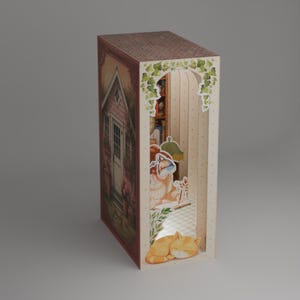 Puede incluir: Diorama de papel decorativo con forma de libro. Presenta una escena de caba&ntilde;a rosa en un lado y un interior acogedor con un gato y una l&aacute;mpara en el otro. El tejado es marr&oacute;n y el interior tiene un ambiente c&aacute;lido y acogedor.