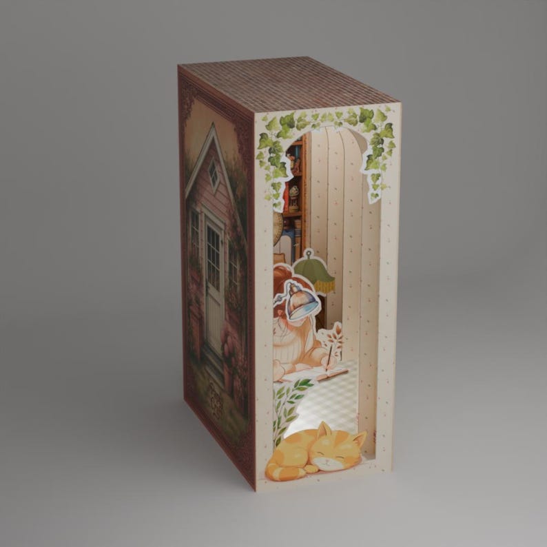Puede incluir: Diorama de papel decorativo con forma de libro. Presenta una escena de caba&ntilde;a rosa en un lado y un interior acogedor con un gato y una l&aacute;mpara en el otro. El tejado es marr&oacute;n y el interior tiene un ambiente c&aacute;lido y acogedor.