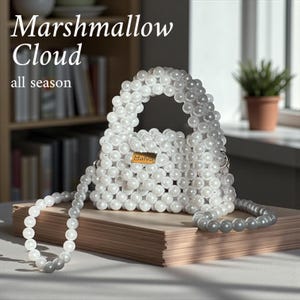 Peut inclure: Un sac à main blanc perlé avec une bandoulière assortie. Le sac a une forme rectangulaire avec une poignée et une petite étiquette dorée qui dit "Malva". Le texte "Marshmallow Cloud all season" est en haut à gauche.