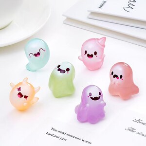 Puede incluir: Seis pequeñas figuras de fantasmas translúcidas en varios colores pastel, incluyendo verde menta, rosa claro, amarillo pálido, verde lima, lavanda y melocotón. Cada fantasma presenta una expresión facial única con ojos y boca de color negro.