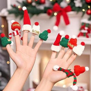 May include: A collection of miniature knitted Christmas-themed finger puppets including red and white Santa hats, green beanies, and striped scarves. Each piece features a small white pom-pom on top, and some items are embroidered with the word LOVE.