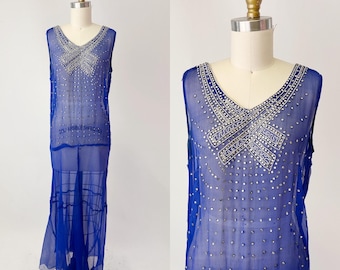 May include: A vintage blue sleeveless dress with a V-neckline, embellished with silver-colored beads. The sheer fabric drapes to the floor, creating a flowing silhouette. The dress is displayed on a mannequin. The text "COLLAPSIBLE SHOULDER" is visible.