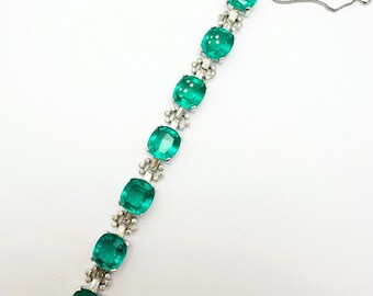 May include: A silver bracelet with a chain closure features a row of emerald green glass stones set in silver.