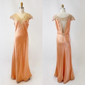May include: A peach-colored, floor-length vintage dress with a V-neckline and cap sleeves. The dress features delicate lace and embroidery around the neckline and hem. The back of the dress has a low V-shaped opening.