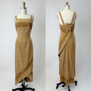 May include: A long, brown, sleeveless dress with a high neckline and a fitted bodice. The dress has a wrap-style skirt with a high-low hemline. The dress is decorated with gold beading and embroidery.