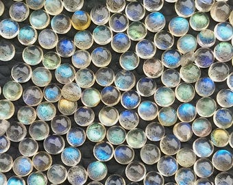 May include: A collection of small, round gemstones with a polished finish. The stones display a range of colours, including blues, greens, and yellows, with iridescent flashes. The gemstones are arranged closely together, creating a dense cluster.
