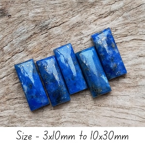 Op de afbeelding: Vijf rechthoekige lapis lazuli stenen met een diepblauwe kleur en gouden vlekken, op een houten oppervlak. De tekst onderaan luidt: Maat - 3x10mm tot 10x30mm. De stenen meten van 3mm x 10mm tot 10mm x 30mm.