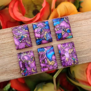 Puede incluir: Seis cabujones rectangulares con un patrón de mosaico de fragmentos de piedra morados y azules unidos por finas vetas metálicas de color dorado. Cada pieza muestra una superficie pulida y plana con formas geométricas variadas y colores.