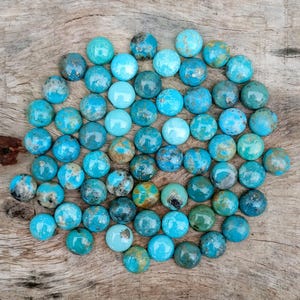 Può includere: Una collezione di pietre preziose rotonde di colore turchese, con varie sfumature di blu e verde. Le pietre sono disposte su una superficie di legno, mostrando le loro trame e motivi naturali. Adatte per la creazione di gioielli.