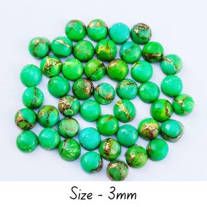 Può includere: Una collezione di piccole perline rotonde verdi con venature color oro. Le perline sono sparse su una superficie bianca. Il testo "Size - 3mm" è in basso nell'immagine.
