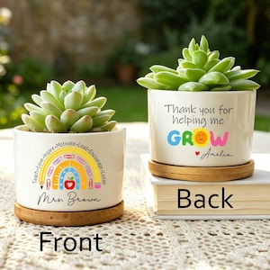 May include: Two white ceramic plant pots with succulents, each on a bamboo coaster. One pot has a rainbow design with text: "Teach-Love-Inspire-Motivate-Lead-Encourage-Listen" and "Mrs. Brown." The other says "Thank you for helping me GROW" and "Amelia."