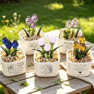 May include: Five white ceramic square planters filled with small pebbles and glass tulip flowers in blue, purple, light pink, and yellow. Each planter features black printed text, including phrases like 'It takes a big heart to shape little minds' and 'Mrs. Smith'.