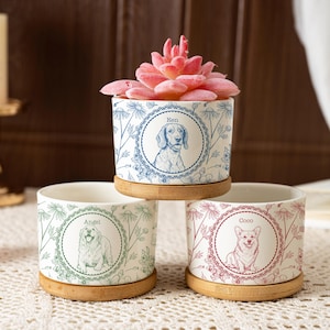 May include: Three cylindrical white ceramic planters with bamboo bases, each featuring a unique dog illustration inside a circular frame and a floral pattern. The top planter holds a pink succulent, while the others are empty.