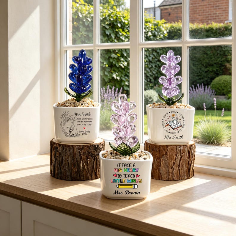 May include: Three white ceramic planters on wooden log bases, each containing a glass flower sculpture. The planters feature printed text and graphics, including 'Mrs. Smith', 'Love, Emily 2021', 'It take a big heart to teach little minds', and 'Mrs. Brown'.