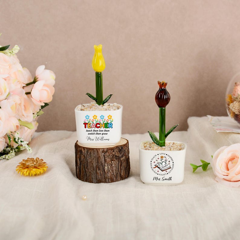 May include: Two white square planters containing glass flowers. The left planter features a yellow tulip and text reading TEACHER teach them love them watch them grow Mrs. Williams. The right planter has a dark flower and a book graphic with Mrs. Smith.