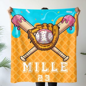 Op de afbeelding: Een honkbal-thema deken met een dessert ontwerp. Het heeft een honkbal, handschoen en gekruiste knuppels, met de honkbal ontworpen als een donut en de knuppels met roze glazuur. De deken heeft de naam "MILLE" en het nummer "23".