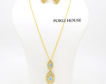 May include: A gold-colored jewelry set featuring a necklace and earrings. The necklace has a pendant with two turquoise-colored stones. The earrings have a similar design. The jewelry is displayed on a white mannequin. The text "POKLI HOUSE" is visible.