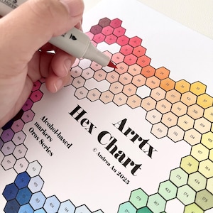 May include: A hand using a grey alcohol-based marker to colour a hexagon on a colour chart. The chart, titled "Arrtx Hex Chart," displays various coloured hexagons with numbers. The chart is labelled "Oros Series" and "Alcohol-based markers."