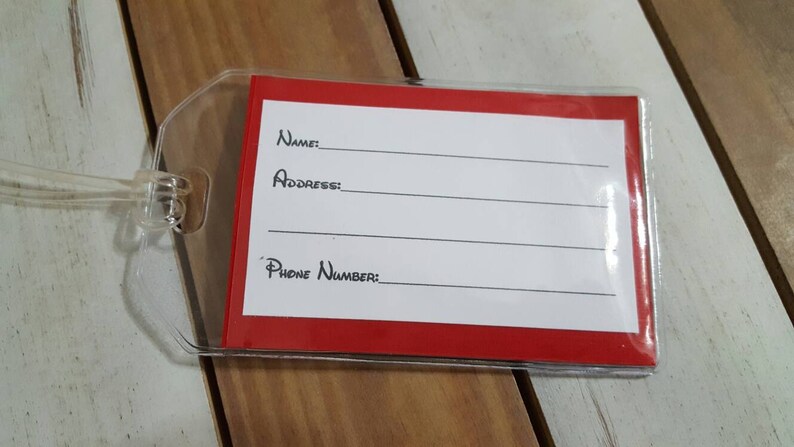 May include: A red luggage tag with a clear plastic cover. The tag has white lines for writing "Name", "Address", and "Phone Number".