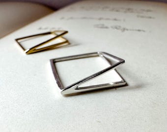 May include: Two geometric rings, one in a polished silver tone and one in a gold tone. Each ring features a square base with an angled, raised bar that connects to one corner, creating a three-dimensional, open-frame structure with clean lines.